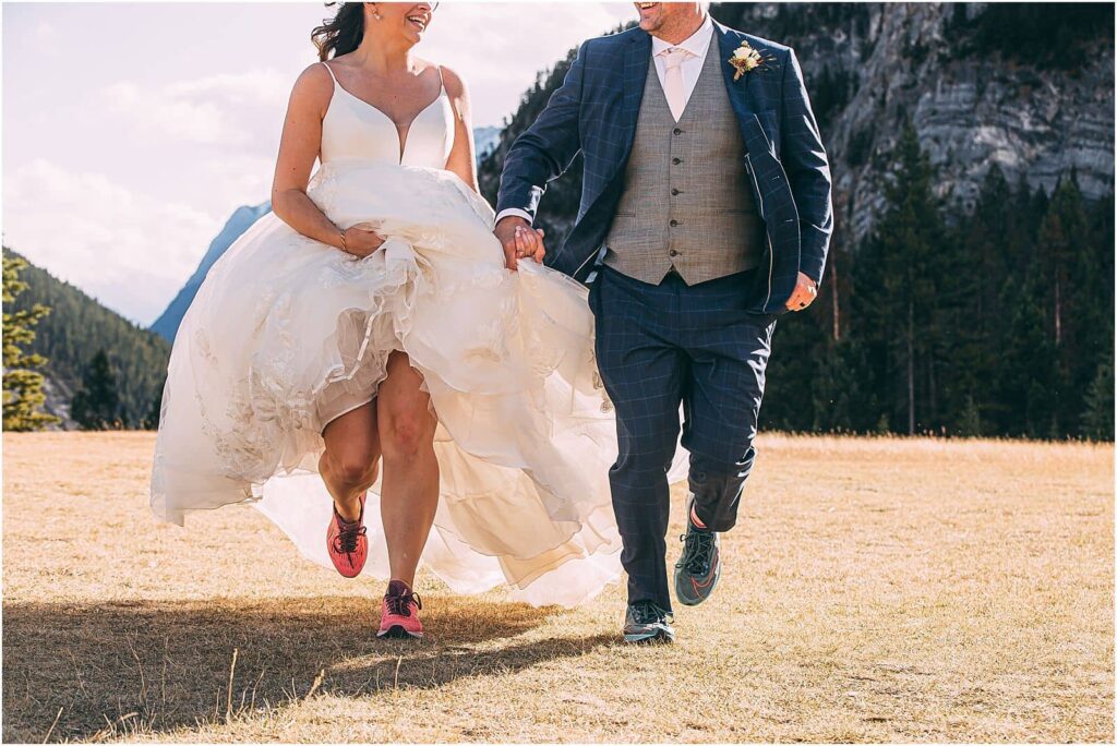bride in groom in their running shoes, holding hands, running on an alpine meadow - elope in your dream location