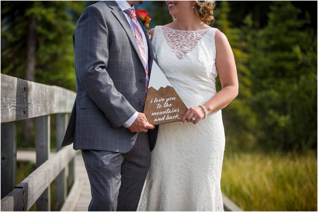 bride and groom holding a handmade sign in the shape of a mountain that says "I love you to the mountains and back"