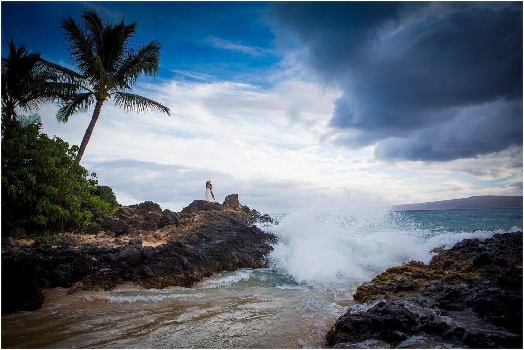 bride and groom atop some rocks along a secluded beach above a crashing surf on the rocks -elope in your dream location