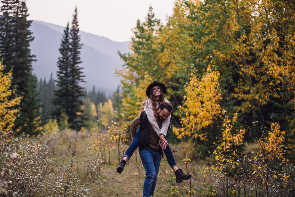 A sweet fall engagement photo of a man giving his partner a piggy back ride