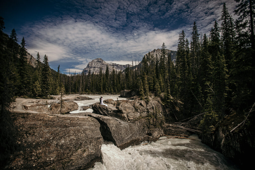 Couple eloping at Natural Bridge in Yoho National Park with rushing glacial water and dramatic mountain scenery.
