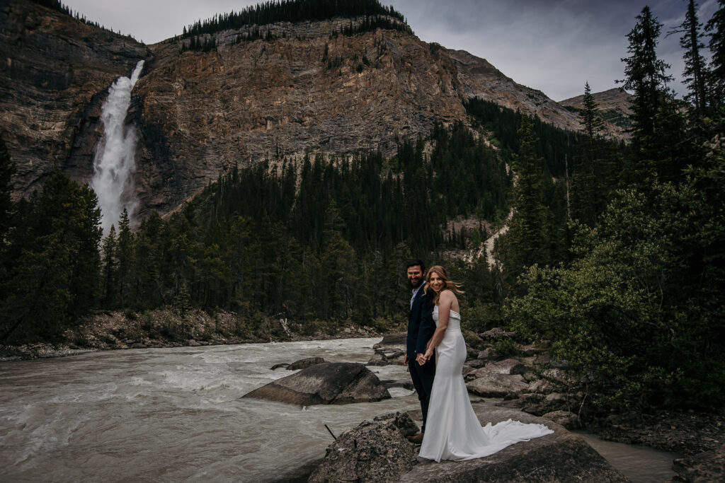 Couple eloping beside a secluded waterfall in the Canadian Rockies surrounded by lush forest.