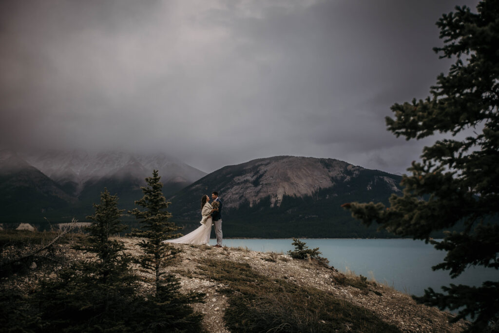 Couple eloping at Abraham Lake  on foggy, snowy day; also known for frozen ice bubbles and snowy mountain scenery, as well as stunning turquoise water and towering evergreens.