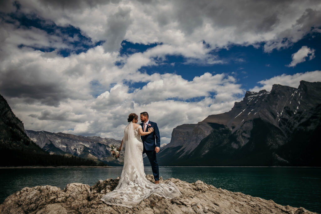 Couple eloping at Lake Minnewanka on a summer afternoon with turquoise water and dramatic mountain scenery.