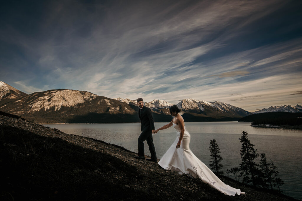 Couple climbing a mountain beside a large turquoise lake during an adventure elopement in the Canadian Rockies.