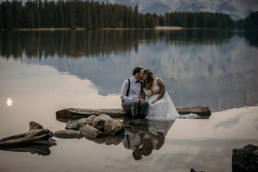 Couple sitting in the shallow water at Two Jack Lake with a perfect mountain reflection during an intimate elopement near Banff.